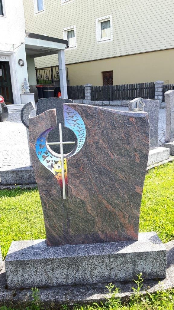 Grabstein mit Kreuzmotiv, mehrfarbigen Akzenten, auf einem Steinsockel, für den Außenbereich.