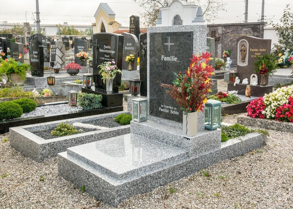 Friedhofsszene mit mehreren Granitgrabsteinen und Grabmarkierungen, viele davon mit Blumen und Laternen.