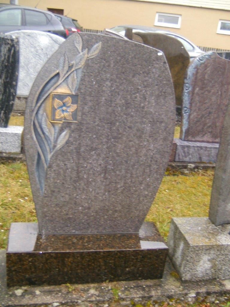 Granitgrabstein mit floralem Dekor, brauner Sockel, im Freien ausgestellt.