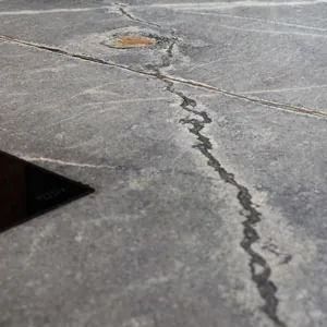 Nahaufnahme einer rissigen, grauen Steinoberfläche mit einem dunklen, gewundenen Riss, der sich darüber erstreckt.