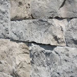 Nahaufnahme einer Steinmauer. Die Steine sind grau und beige, mit rauer Oberfläche und unregelmäßigen Formen.