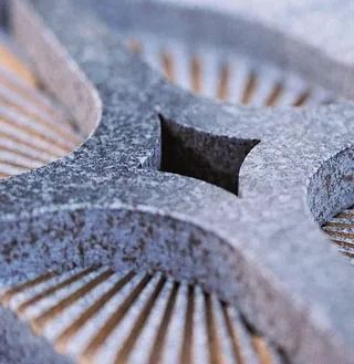 Nahaufnahme eines verwitterten, grauen Metallbauteils einer Schleifmaschine mit einem quadratischen Loch und radialen Nuten.