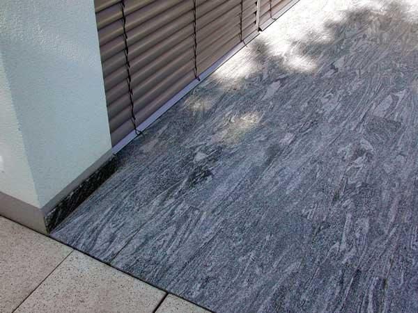 Eine Rampe aus grau gemustertem Stein führt zu einem Gebäude mit einer Fassade aus Metallrollläden.