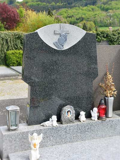 Grabstein mit Kreuz, betenden Händen und Engelsfiguren auf einem Friedhof.