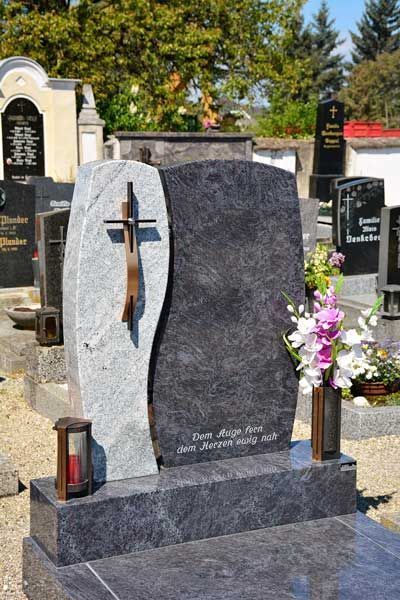 Grabstein mit einem Kreuz und einem Blumenstrauß auf einem Friedhof.