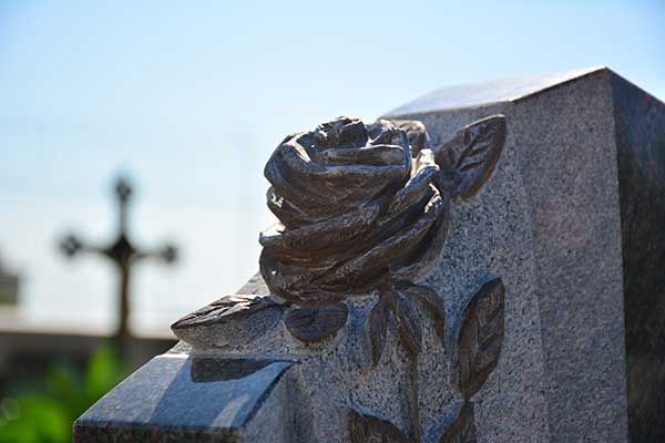 Nahaufnahme eines Granitgrabsteins mit einer eingravierten Rose, im Hintergrund ein Kreuz.