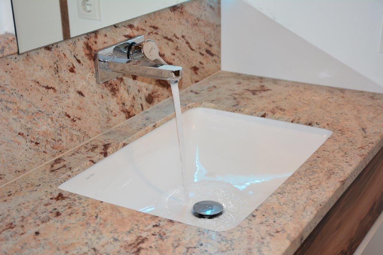 Badezimmerwaschbecken mit fließendem Wasser, Granit-Arbeitsplatte, Chromarmatur und weißem Becken.