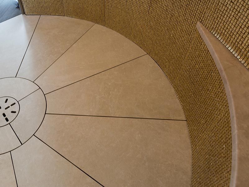 Hellbrauner Fliesenboden mit radialem Muster und gewebte Wand, die sich um den Rand herum wölbt.