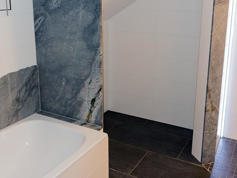 Badezimmer mit dunklem Fliesenboden, weißer Badewanne und grauen Marmor-Akzentwänden.