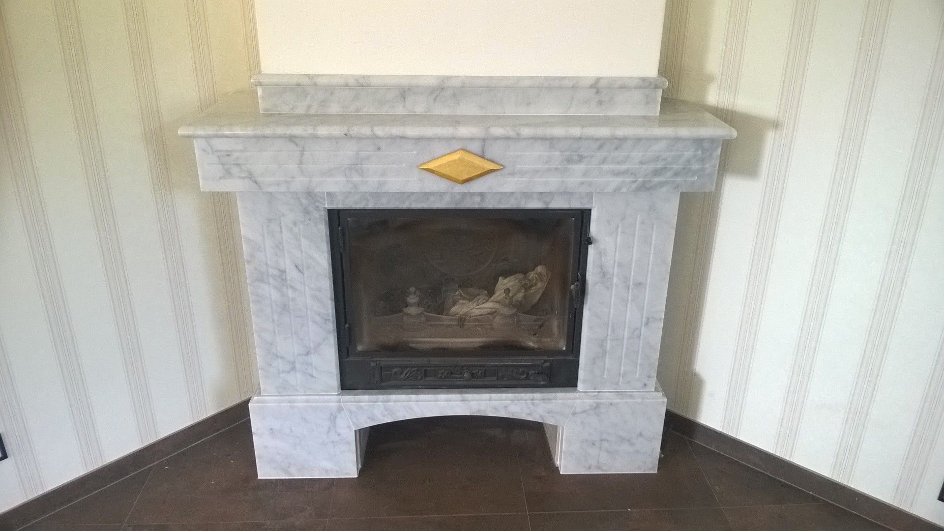 Marmorkamin mit goldenen Akzenten, in einer Ecke eines Zimmers mit gemusterter Tapete und dunklem Bodenbelag.