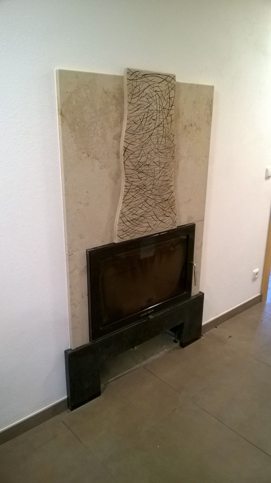 Kamin mit dunklem Rahmen und Einfassung vor heller Steinwand, dunkler Boden.