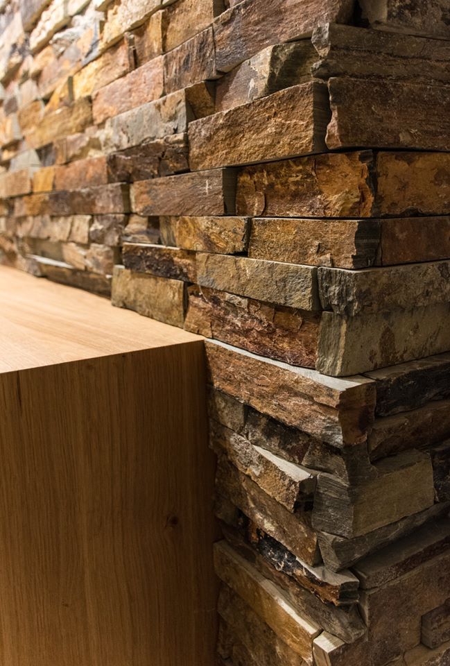 Ecke mit Steinmauer neben einem hellen Holzschrank. Dunkelbraune, beige und goldene Farbtöne.