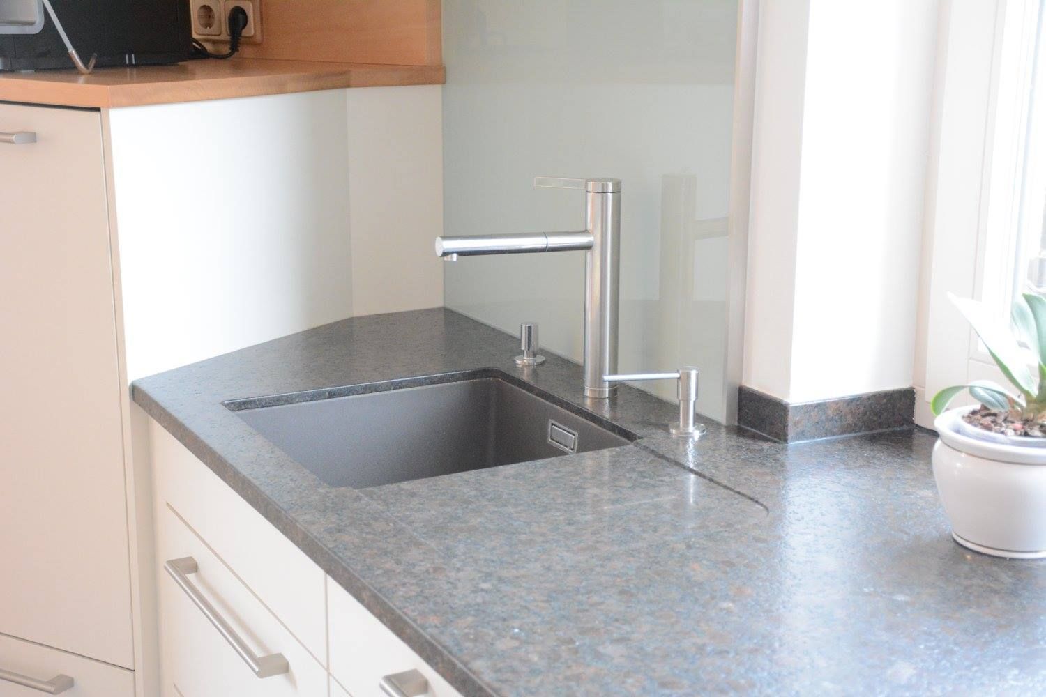 Eckküchenspüle mit moderner Armatur, Granitarbeitsplatte, hellblauem Fliesenspiegel und weißen Schränken.