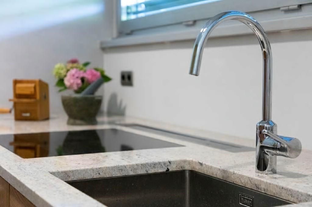 Küchenspüle mit Chromarmatur, Granitarbeitsplatte, Blumen und eingebautem Kochfeld.