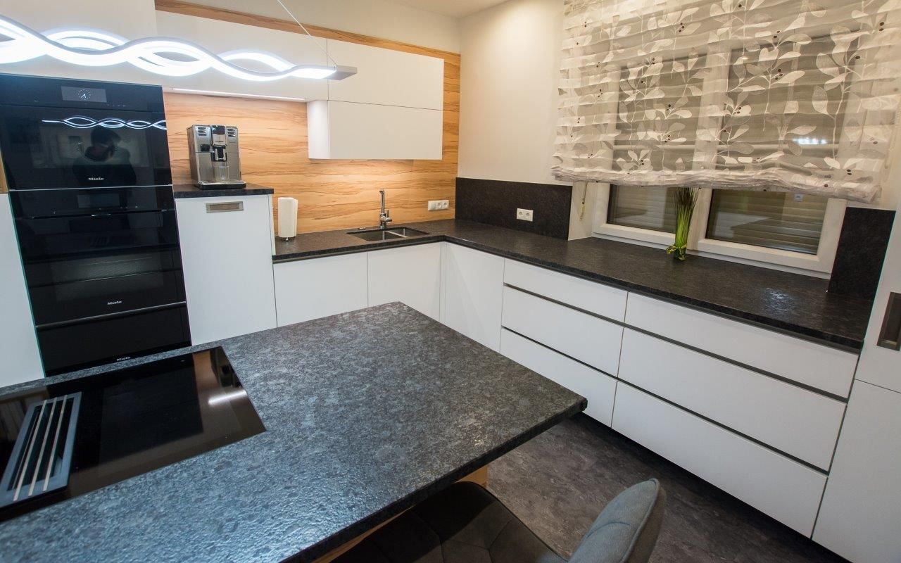 Moderne weiße Küche mit schwarzen Arbeitsplatten, Einbaugeräten und einer Kochinsel.