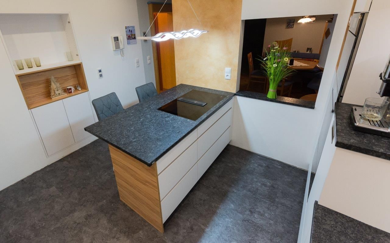 Kücheninsel mit Kochfeld, zwei Barhockern und Blick in den Essbereich.