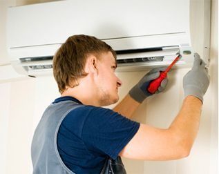 Un técnico usando un destornillador para reparar un aire acondicionado de pared