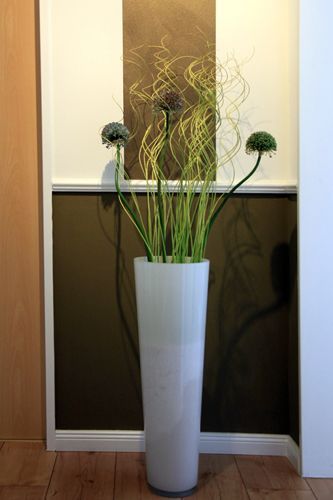 Eine große weiße Vase voller Blumen steht auf einem Holzboden.