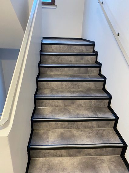 Eine Treppe mit weißem Geländer und grauem Fliesenboden.