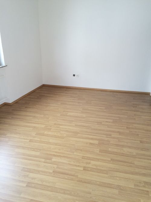 Ein leerer Raum mit Holzboden und weißen Wänden.