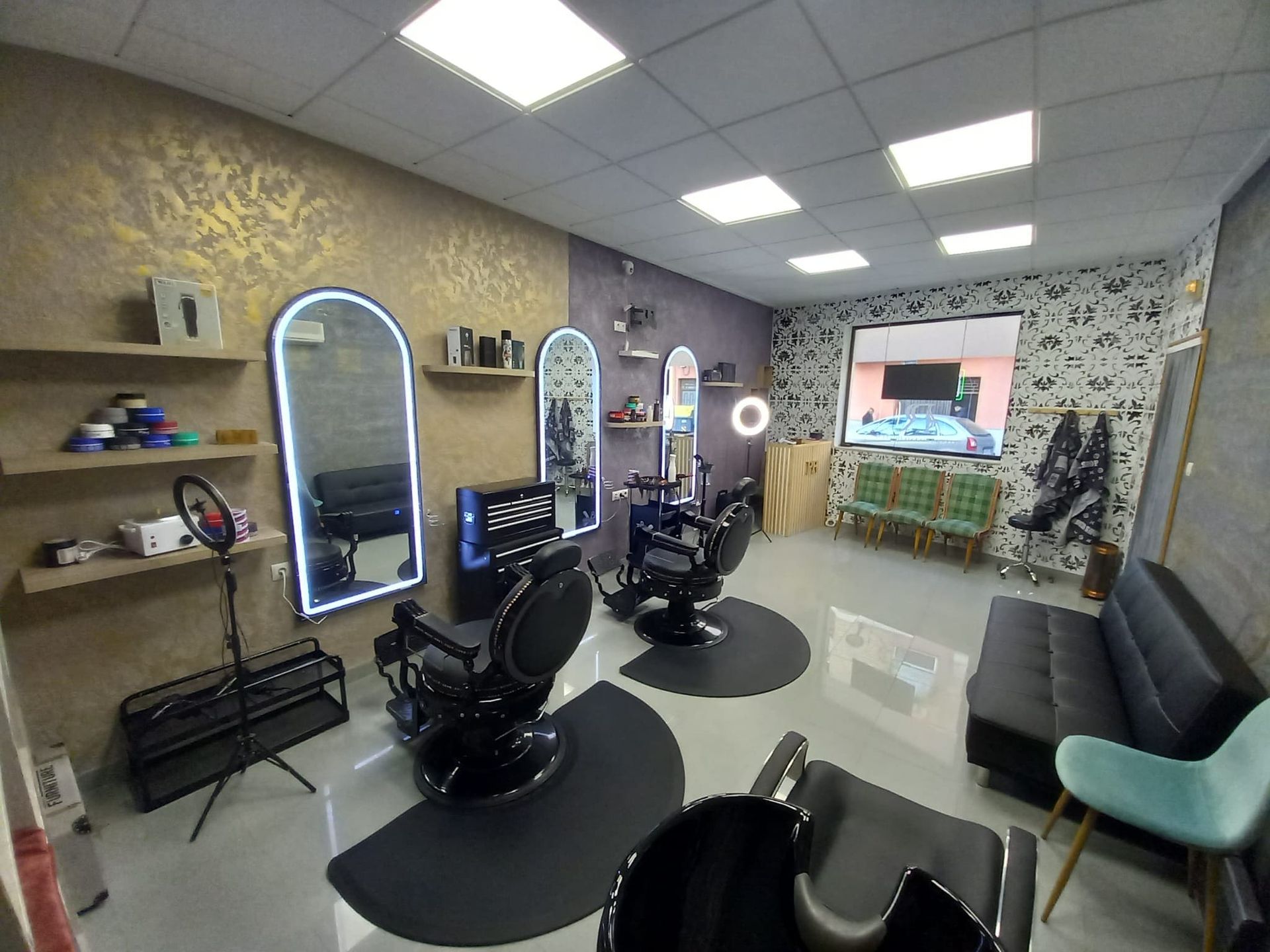 Interior de una peluquería con dos sillones de peluquería negros, espejos arqueados iluminados, estantes para productos y una zona de espera.