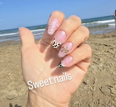 Una mano en la playa muestra un diseño de uñas con puntas de estampado de leopardo y un detalle de estrella dorada, con el texto 