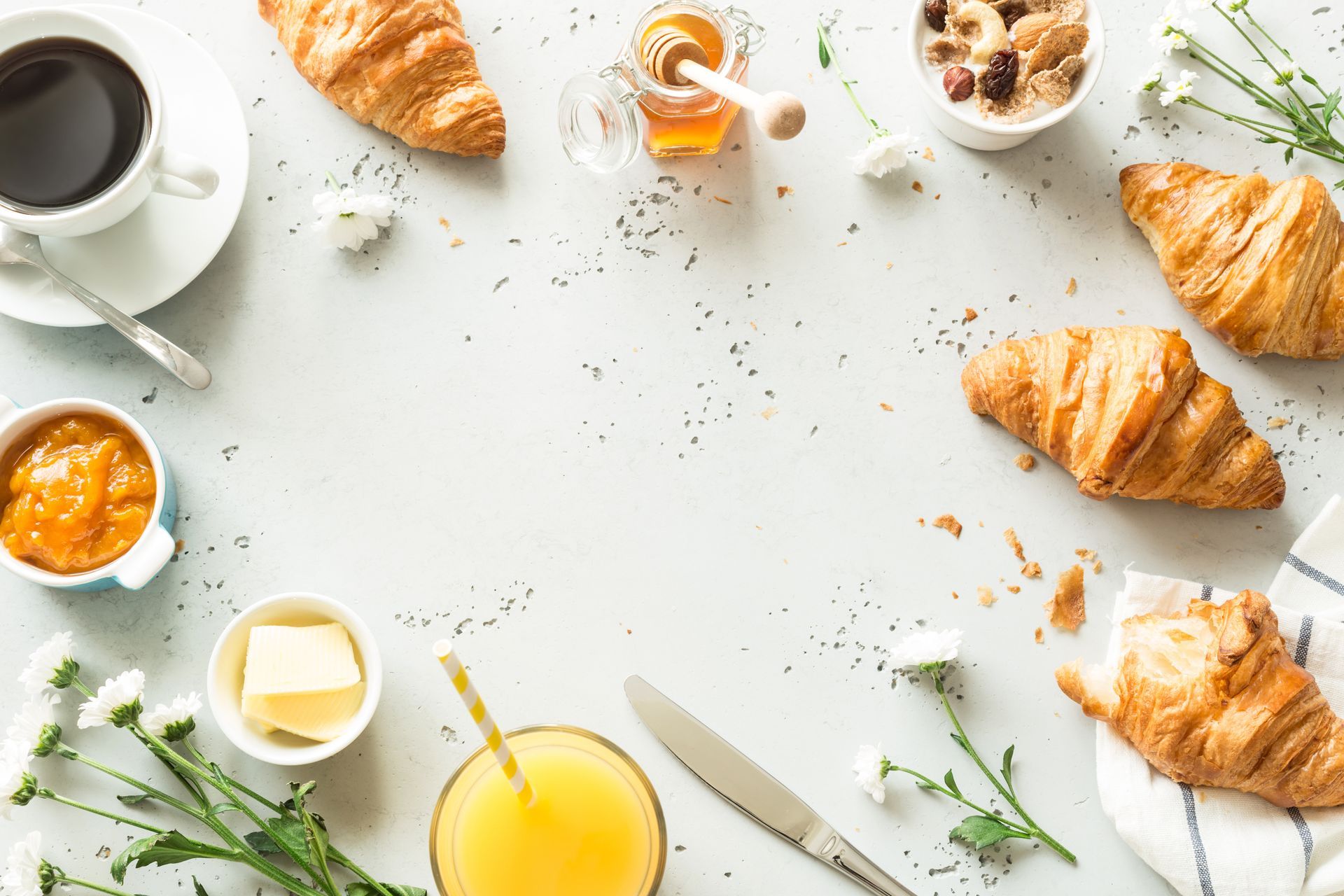 Petit-déjeuner composé de croissants, de café, de jus d'orange et d'herbes aromatiques sur une table légère.