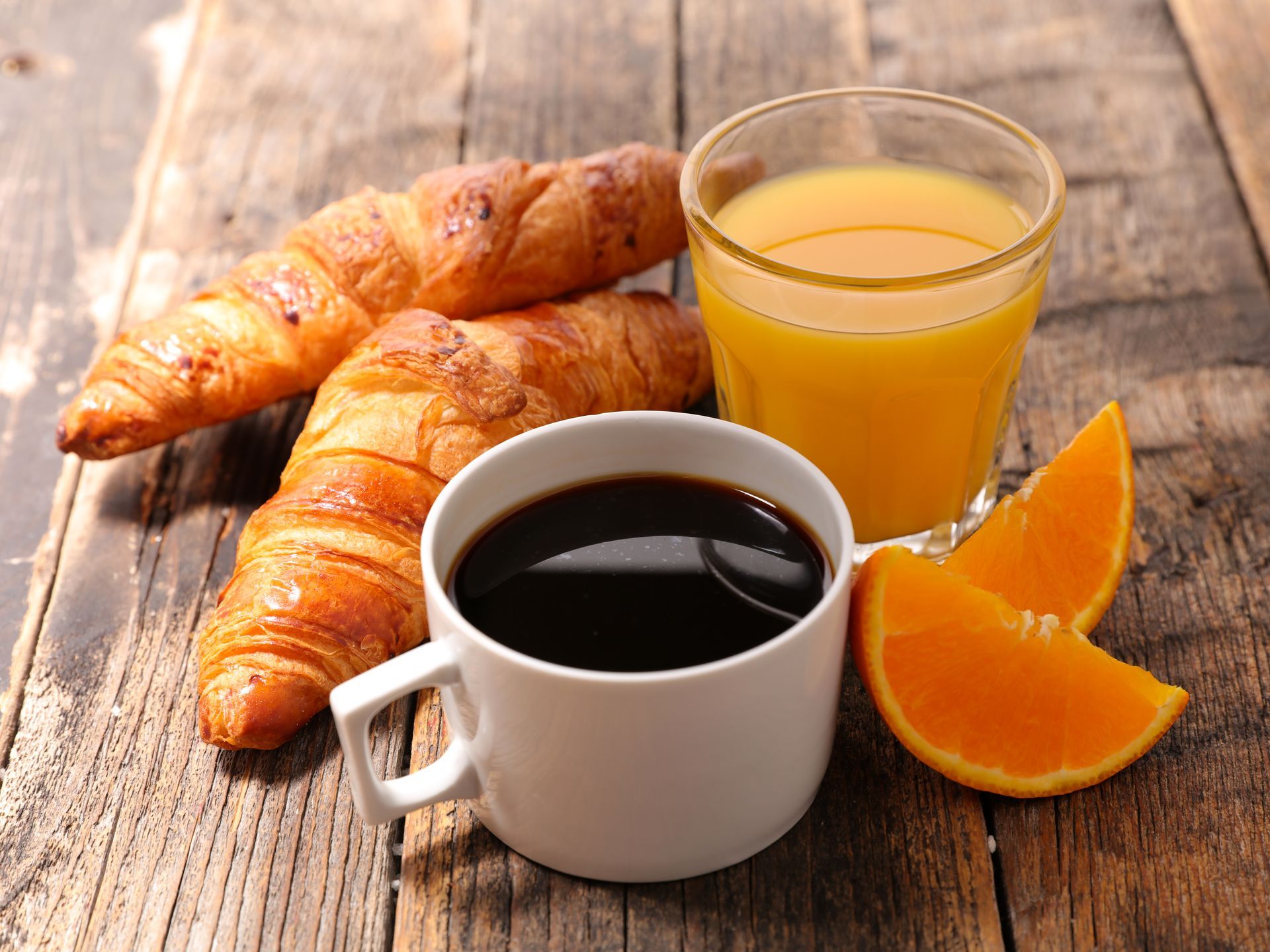 Café, jus d'orange, croissants et tranches d'orange sur une table en bois.