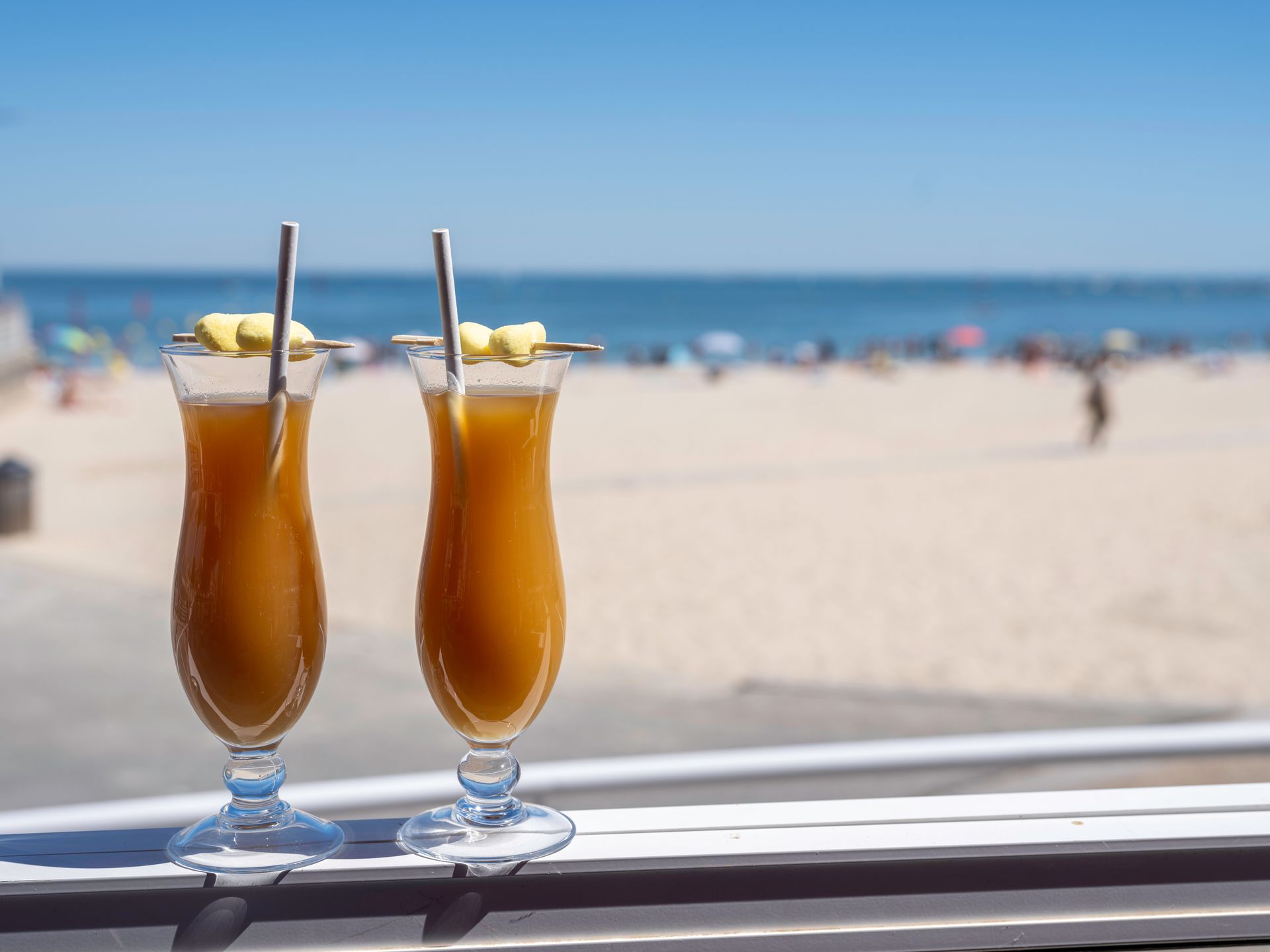 Deux cocktails tropicaux avec pailles sur une table donnant sur une plage ensoleillée et la mer.