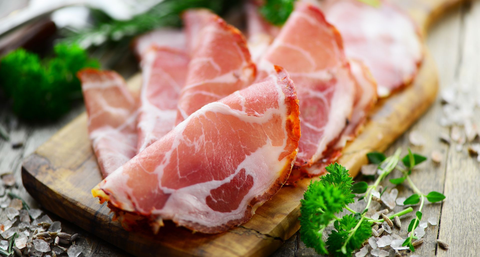 Jambon cru finement tranché sur une planche en bois, garni de persil.
