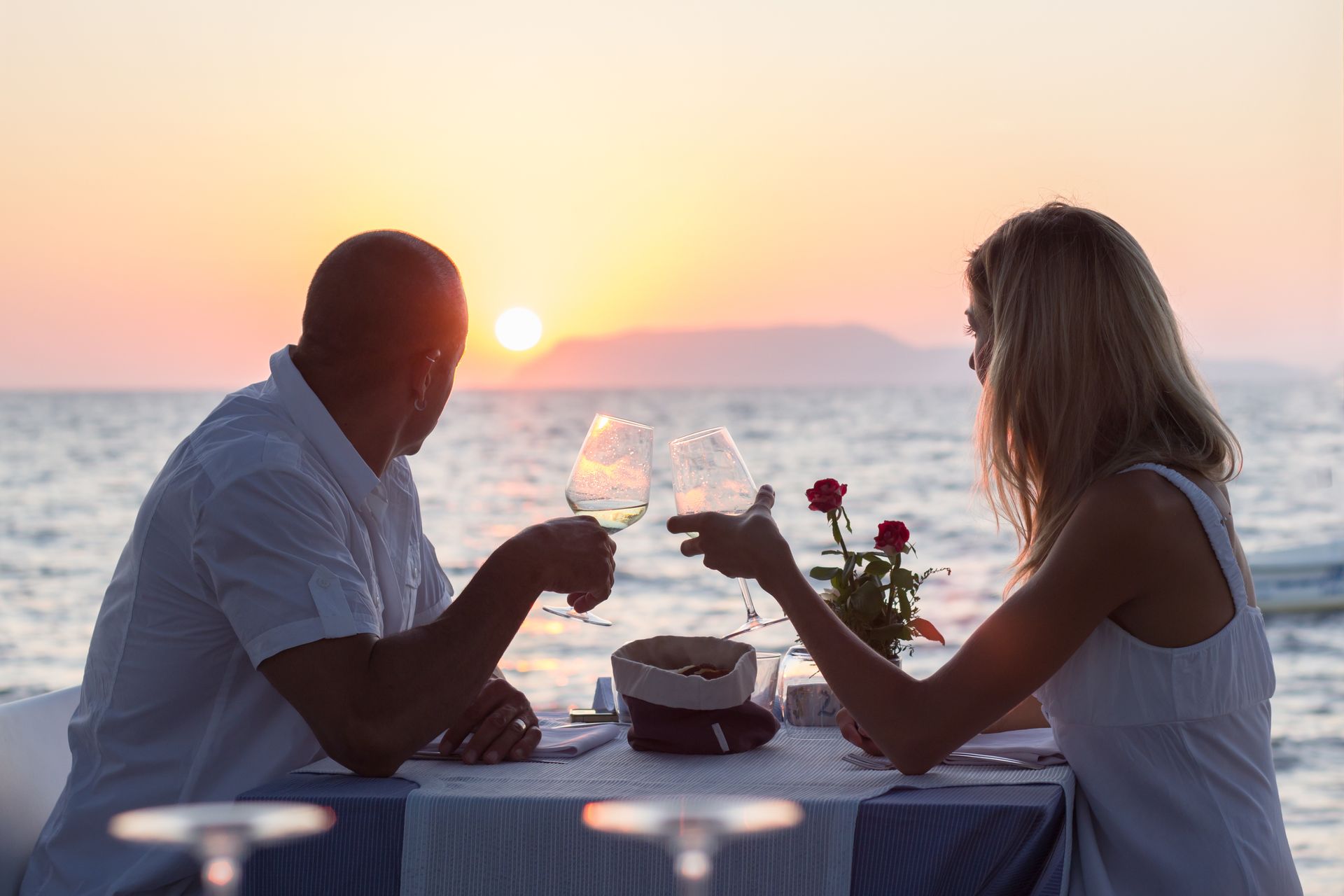 Un couple trinque au vin au coucher du soleil, au bord de la mer.