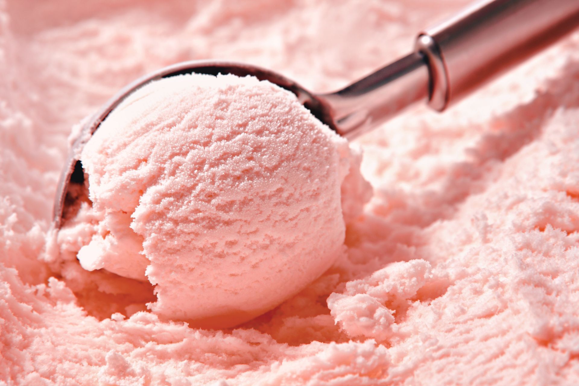 Une cuillère en métal contenant une boule de glace rose sur une surface rose et duveteuse.