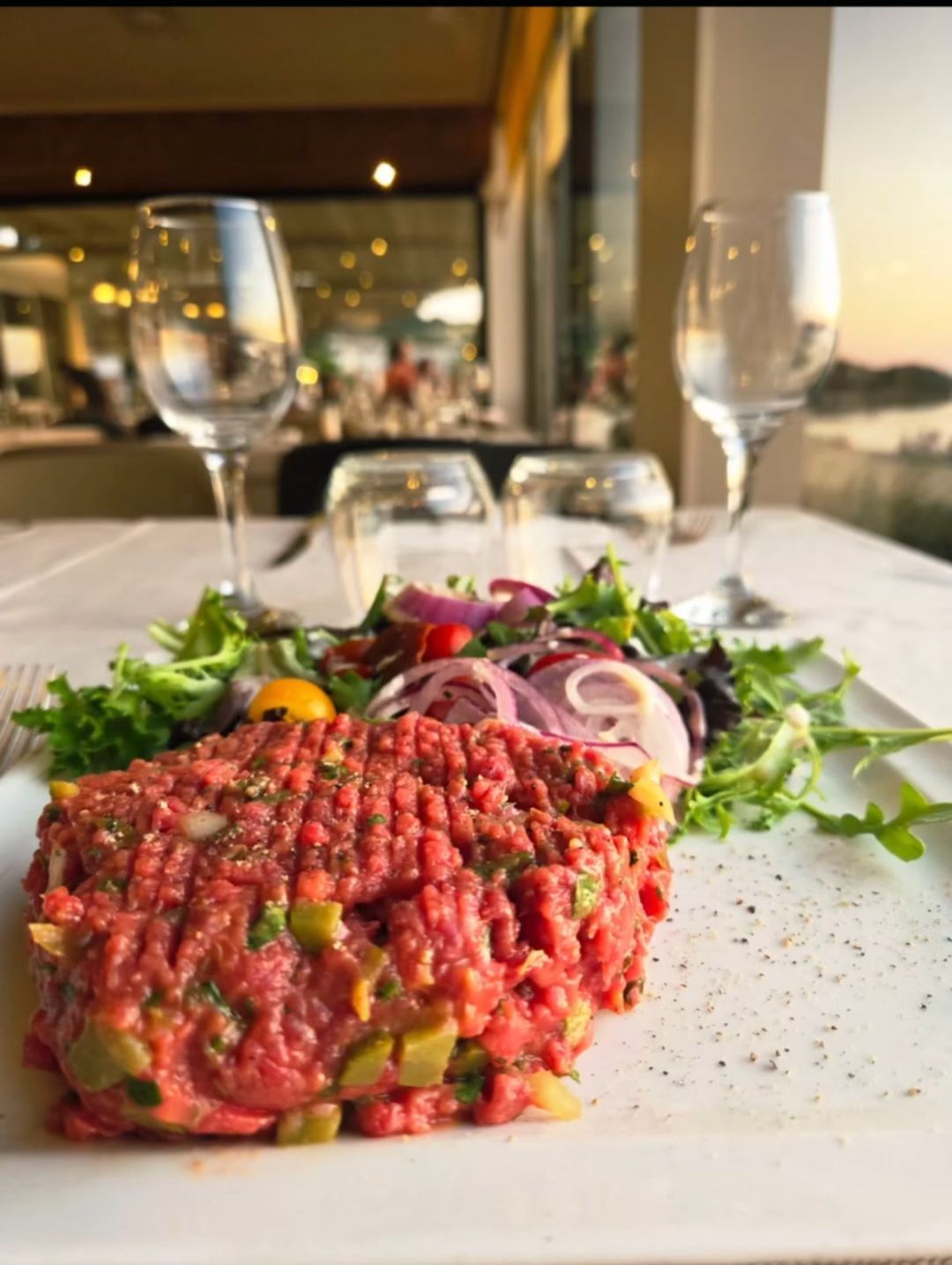 Tartare de bœuf cru sur une assiette blanche avec des légumes verts et des oignons dans un cadre de restaurant