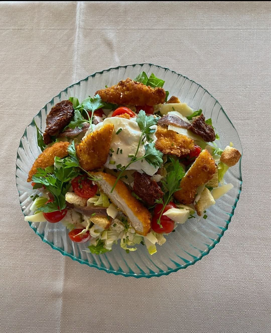 Salade composée dans un saladier en verre avec des lanières de poulet panées croustillantes, des tomates et de la verdure, sur une nappe beige.
