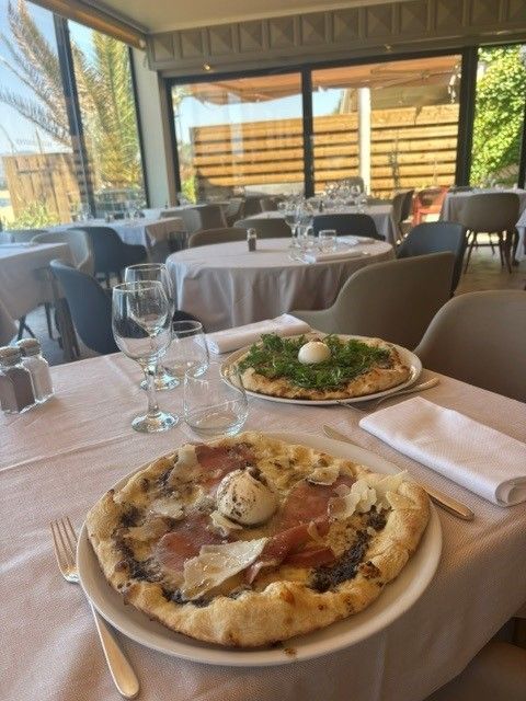 Table de restaurant avec pizza et salade sous une terrasse couverte donnant sur l'eau.