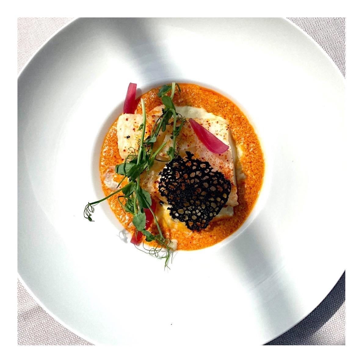 Plat gastronomique présenté sur une assiette blanche, avec sauce à l'orange, caviar noir, herbes et garniture de légumes.