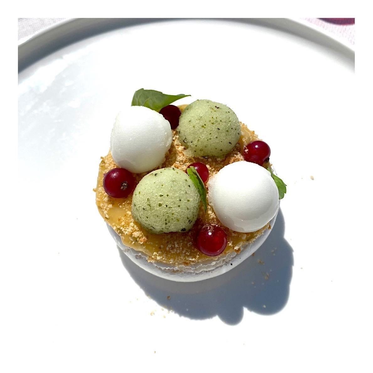Petite tartelette dessert avec des boules blanches et vertes, des baies rouges et de la menthe sur une assiette blanche.