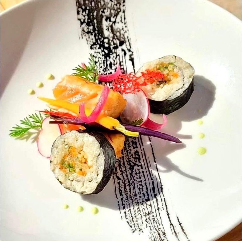 Rouleaux de sushi et sashimis présentés avec une garniture colorée et une sauce noire sur un plat blanc.