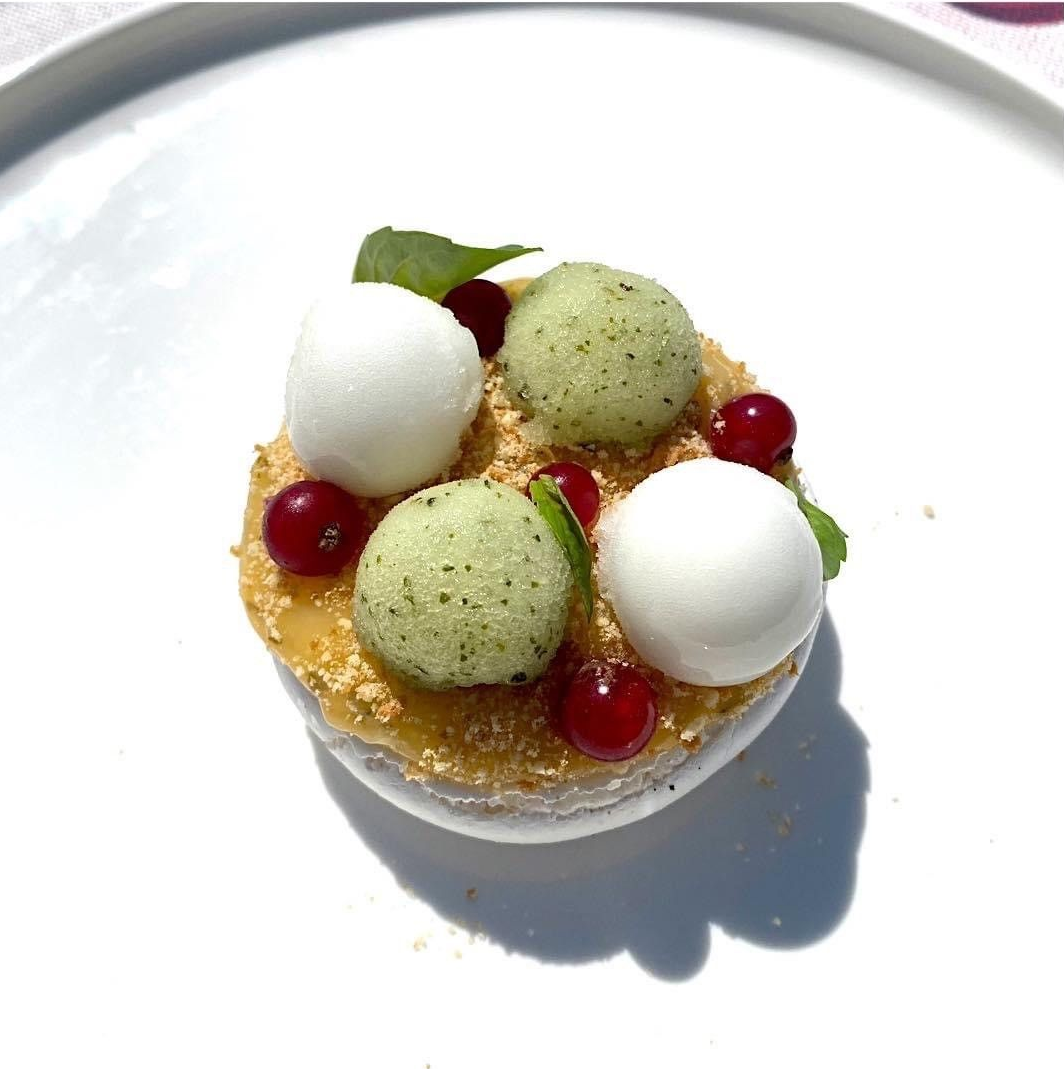 Dessert présenté sur un plat blanc, composé de boules vertes et blanches, de fruits rouges et de miettes.