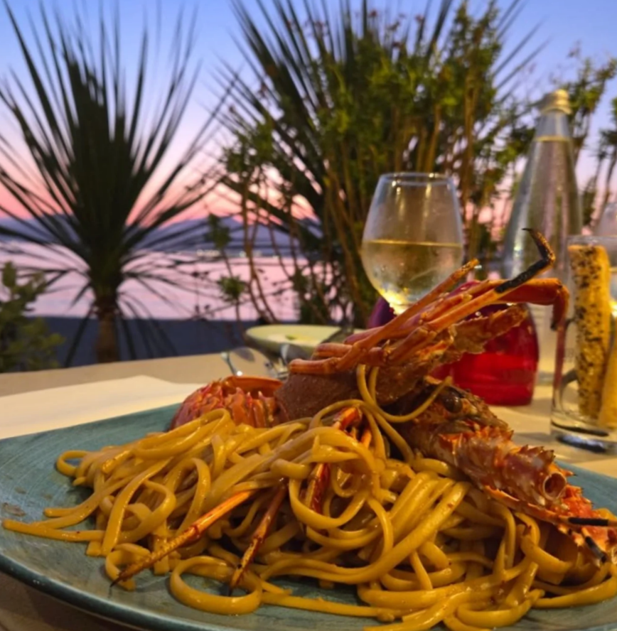 Pâtes au homard sur une table en bord de mer au coucher du soleil.