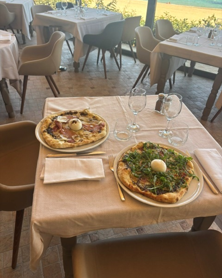 Deux pizzas sur une table à la terrasse d'un café, avec des nappes beiges et des chaises à proximité.
