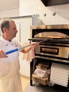 Le cuisinier du restaurant qui enfourne une pizza dans le four.