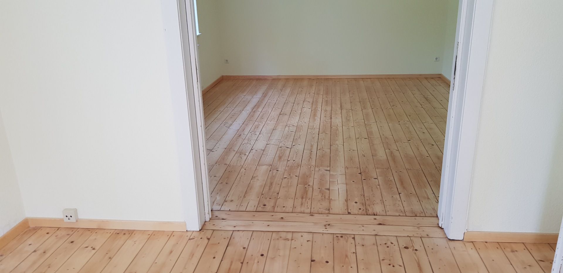 Blick durch eine Türöffnung in einen Raum mit Holzboden. Die Wände sind weiß und hellgrün.