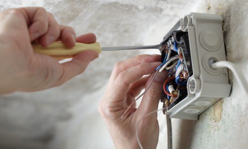 Una persona está fijando una caja eléctrica en una pared con un destornillador.