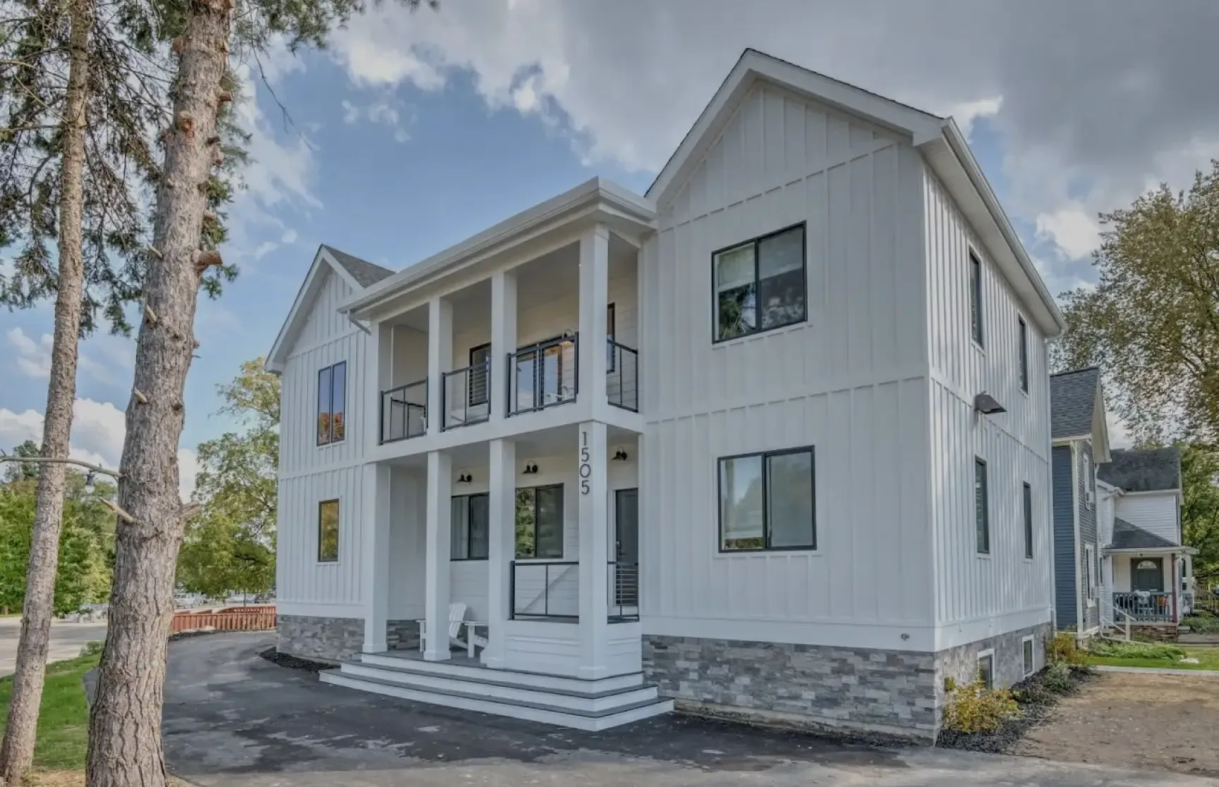 White two-story house with a porch, black windows, and stone base under a blue sky.