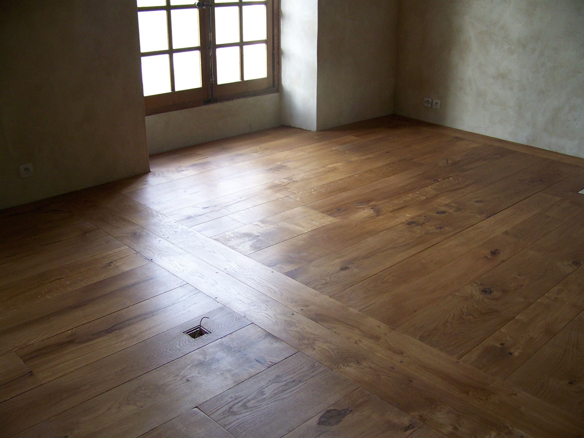 Sol en bois dans une pièce, avec une fenêtre dans le coin supérieur gauche.