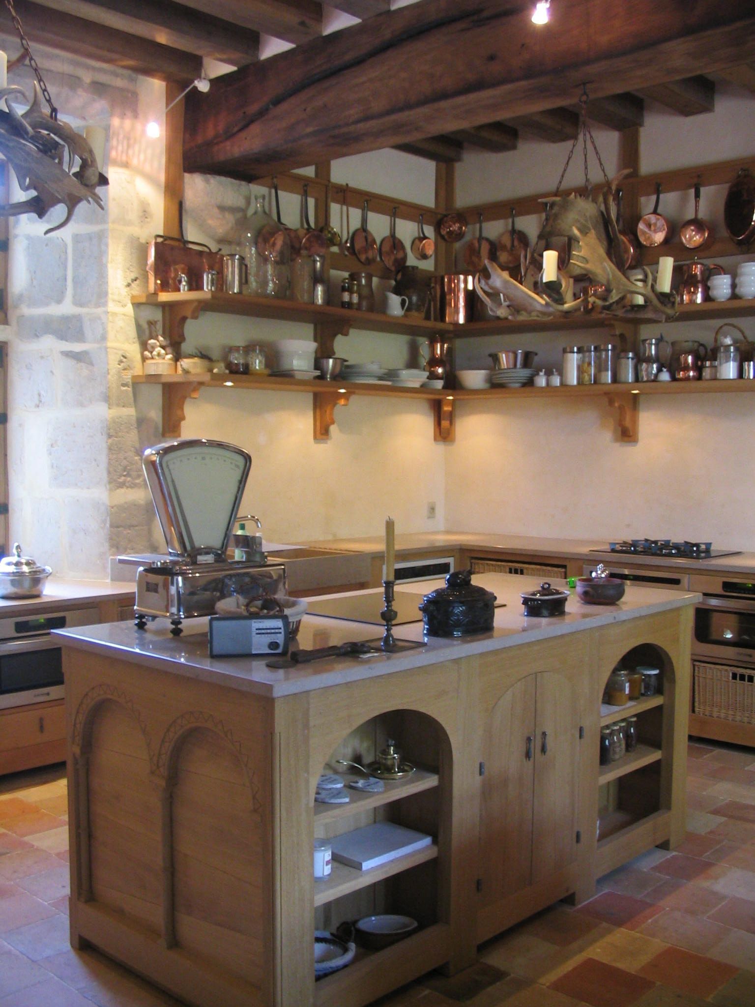 Une cuisine rustique avec un grand îlot central, des ustensiles de cuisine en cuivre et des poutres en bois.