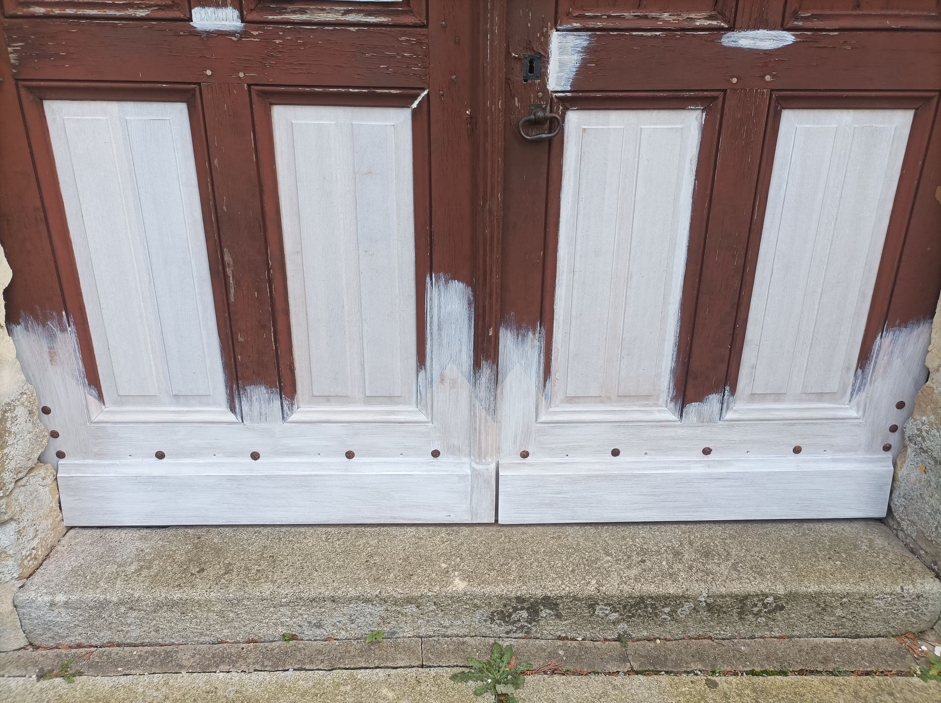 Double porte en bois brun et blanc à la peinture écaillée, montée sur une marche en pierre.