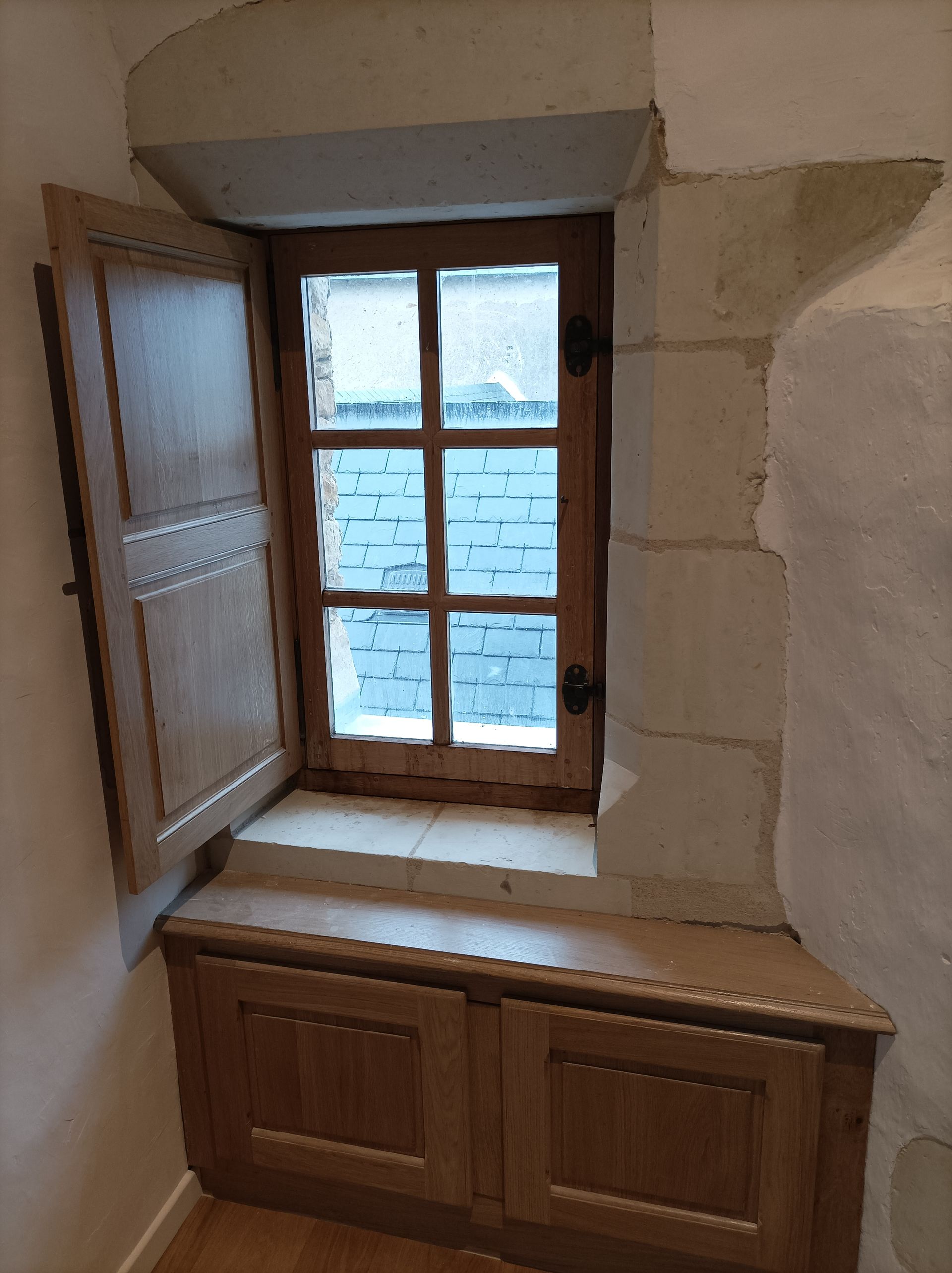 Fenêtre en bois à volet ouvert, encastrée dans un mur en pierre, au-dessus d'une armoire en bois.