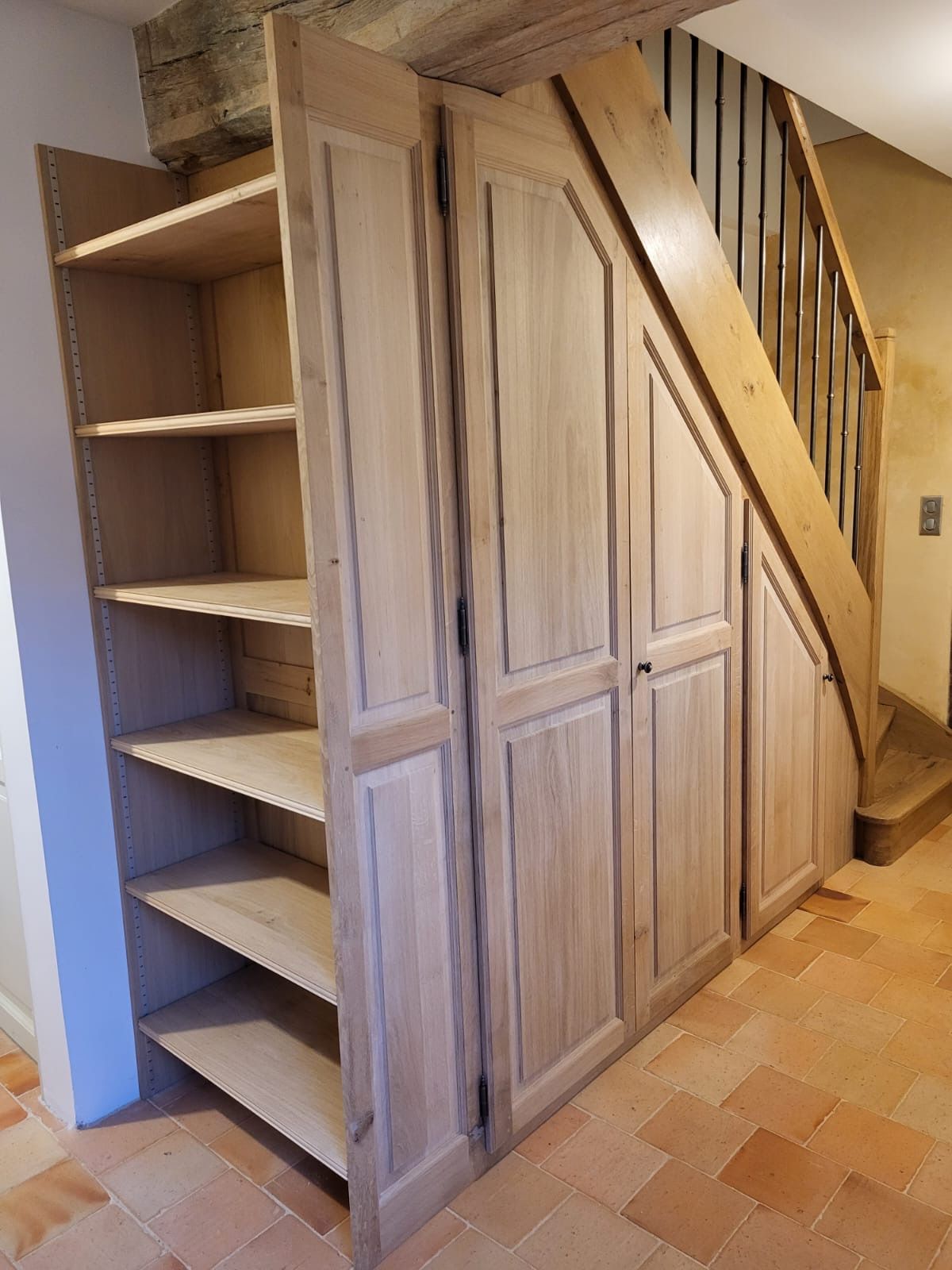 Placards et étagères en bois intégrés au mur à côté d'un escalier, sol en carreaux de terre cuite.